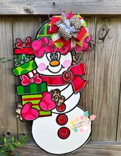 a snowman door hanger hanging on a wooden fence with christmas decorations around it