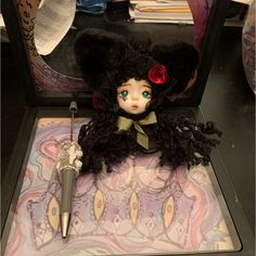 a doll with black hair and green eyes sitting on a table next to an umbrella