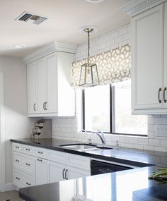 a kitchen with white cabinets and black counter tops in front of a window that has a light fixture hanging from the ceiling