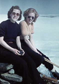 two people sitting on rocks near the water with skis and poles in their hands