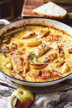 a casserole dish with chicken and cheese in it on a table next to an apple