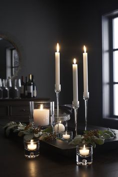 candles are lit on a tray with greenery