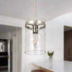 a glass light fixture hanging from a ceiling in a kitchen with white counter tops and cabinets