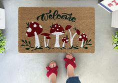 Welcome guests into your home with a whimsical touch! This Retro Mushrooms Doormat features a playful design of red and white mushrooms with green text. The original design will add a quirky charm to your doorstep.  Product Overview The perfect doormat for a fun theme. An affordable, ideal housewarming gift for newlyweds or your friends. Available in 3 sizes; Small, 16x24 inches, Standard size, 18 x 30 inches and Oversized, 24x36 inches to fit most doors. Hand made in the USA from natural coir fibers for mold, mildew resistance. Extra durable, thick vinyl backing ensures no dangerous slippage when used. Permanent ink and UV sealant protects your custom doormat from the elements. Shop our doormat layering rugs here! All our doormats are tan/natural brown in color. The natural coir fibers of Painting Coir Doormat Diy, Diy Welcome Mat Paint, Cute Doormat Ideas, Mushroom Doormat, Diy Doormat Paint, Funny Door Mats, Painted Outdoor Rug, Diy Doormat Ideas, Welcome Mat Ideas