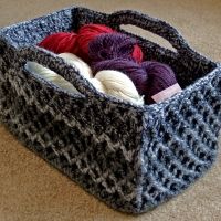 a crocheted basket with yarn in it on the floor next to a carpet