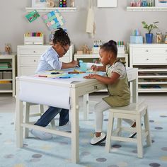 two children sitting at a table playing with their toys in a playroom filled with furniture