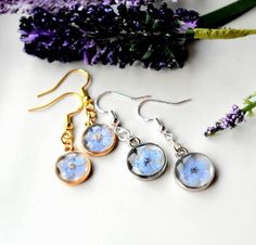 Give her a gorgeous handmade  gift that will always remind her of you! Handmade, preserved, dried pressed Blue Forget Me Not  flower, dangle earrings with  -Sterling silver fish hooks Or - 18k Gold plated Sterling Silver-14mm round -Drop length- 1.25" -domed, glass like surface  -with a real blue forget me not flower suspended in crystal clear resin  -comes with silicone push back closures. -Made with real dried pressed flowers and resin- crystal clear, eco-friendly, and resistant to scratches, Cheap Silver Jewelry With Pressed Flowers, Silver Earrings With Pressed Flowers For Wedding, Silver Wedding Earrings With Pressed Flowers, Wedding Silver Earrings With Pressed Flowers, Blue Dangle Earrings For Mother's Day, Silver Pressed Flowers Earrings For Gift, Silver Pressed Flowers Drop Earrings, Lavender Jewelry With Pressed Flowers For Gifts, Delicate Silver Earrings With Pressed Flowers