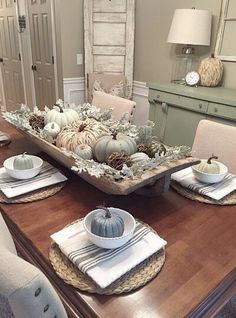 a dining room table with plates and place settings on it, the centerpieces are white pumpkins