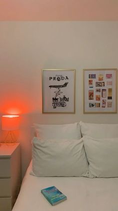 a bed with white sheets and two pictures on the wall above it next to a lamp