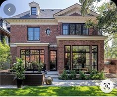 a large brick house with lots of windows and plants in the front yard, on a sunny day