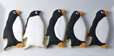 four decorated penguin cookies on a white plate with black and orange icing in the shape of penguins