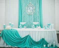 the table is set up with white and blue decorations on it, along with an aqua - green drape