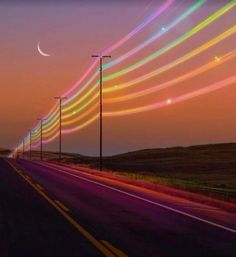 a long line of street lights on the side of a road at night with colorful streaks in the sky