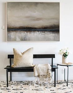 a painting hanging on the wall above a bench with two chairs and a table in front of it