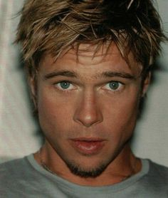 a man with blonde hair and blue eyes looks at the camera while wearing a gray shirt