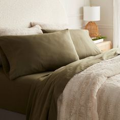 a bed with green sheets and pillows in a room next to a lamp on a nightstand