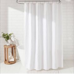 a white shower curtain in a bathroom next to a wooden stool and potted plant