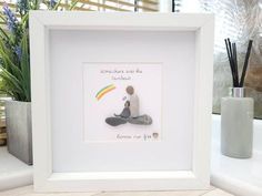 a white frame with a small child holding a rainbow in it's hand, sitting on a counter next to a potted plant