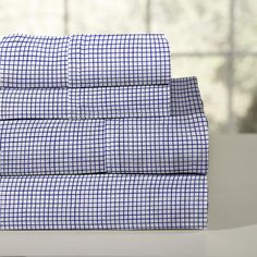 the blue and white checkered sheet set is folded on top of a table next to a window