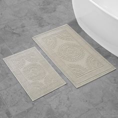 two bathroom rugs sitting on the floor next to a bath tub