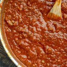 a large pot filled with sauce and a wooden spoon in the bottom left corner, on top of a wood table