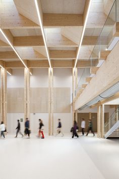 many people are walking around in a large building with wood beams and white flooring