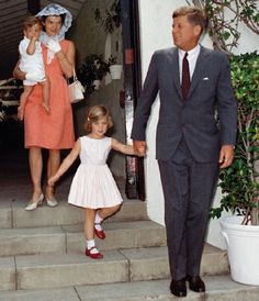 a man and woman holding hands while walking up steps with two children in front of them