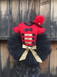 a red shirt and black tutu skirt with gold bow on the top, sitting against a wooden wall