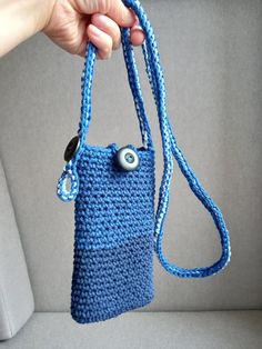 a hand holding a blue crocheted purse with an eye on the front pocket