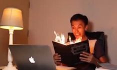 a man sitting in front of a laptop computer while holding an open book with candles on it