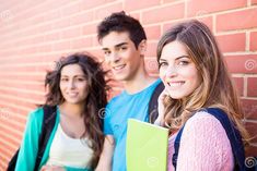 three young people standing in front of a brick wall, one holding a folder and the other smiling