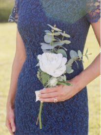 a woman in a blue dress holding a white rose and greenery boutonniere