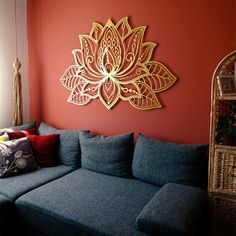 a living room with a gray couch and red wall behind the couch is a large gold flower