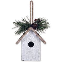 a white birdhouse hanging from a rope with pine cones and evergreen needles on top