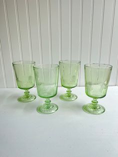 four green glass cups sitting on top of a white table next to a striped wall