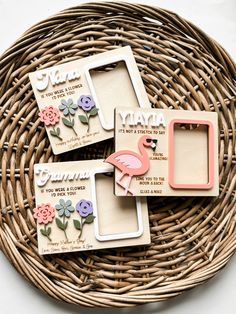 three wooden frames with flowers and a pink flamingo on them sitting in a wicker basket