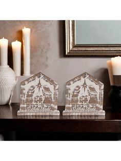 two small wooden houses sitting on top of a table next to candles and a vase