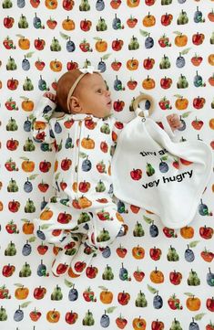 a baby laying on top of a bed next to a white bag with fruit on it