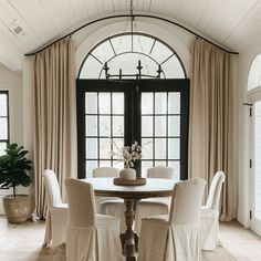 a dining room table with white chairs and a potted plant in the center surrounded by windows