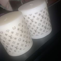 two white candles sitting next to each other on top of a black table with louis vuitton designs