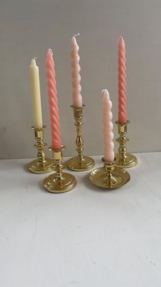 four candles are lined up next to each other on a white table top with gold bases