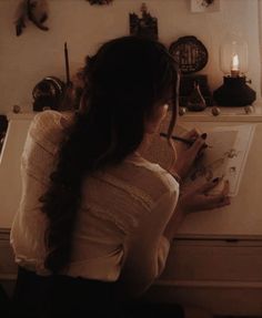 a woman sitting at a desk writing on a piece of paper with a candle in front of her