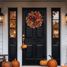 a black front door with two pumpkins on the steps and lanterns hanging from it