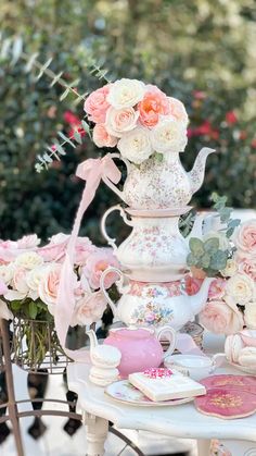 a table topped with pink and white flowers next to a tea pot filled with roses