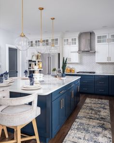 a large kitchen with blue cabinets and white counter tops, gold pendant lights over the island