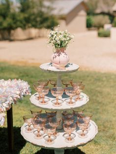 a three tiered cake stand with wine glasses on it and flowers in the vase