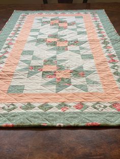 a quilted table runner on top of a wooden table with chairs in the background