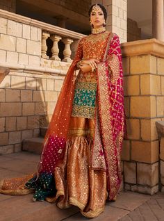 a woman in a colorful outfit standing next to a brick wall and stone steps with her hands on her hips