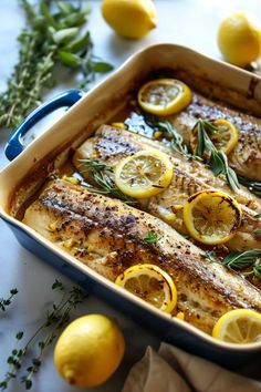 baked fish with lemons and herbs in a blue casserole dish