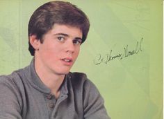 a young man is sitting in front of a green wall